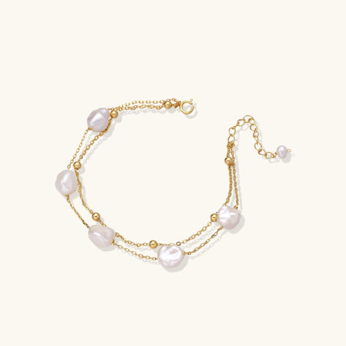 Double-strand gold bracelet with irregular baroque pearls and smooth freshwater pearls on cream background.