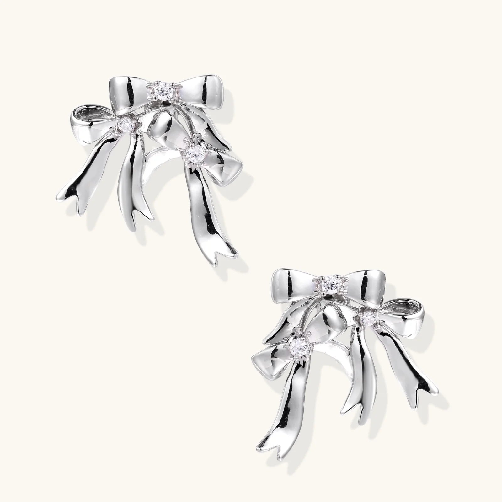 Sculptural bow earrings in polished white gold plate with sparkling zirconia stones and flowing ribbon details