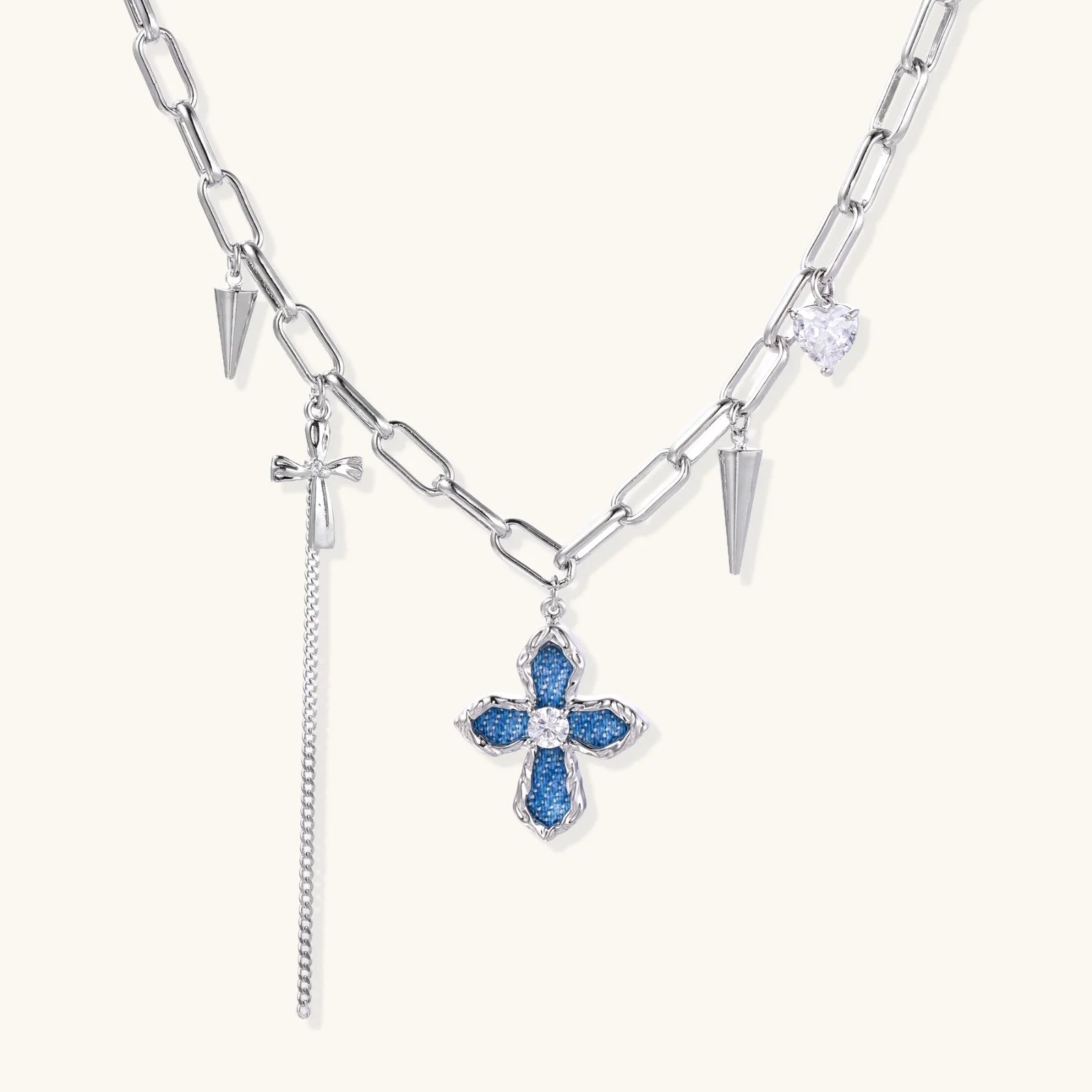 White gold plated chain necklace with blue textured cross pendant, spike charms, and mini cross detail on beige background