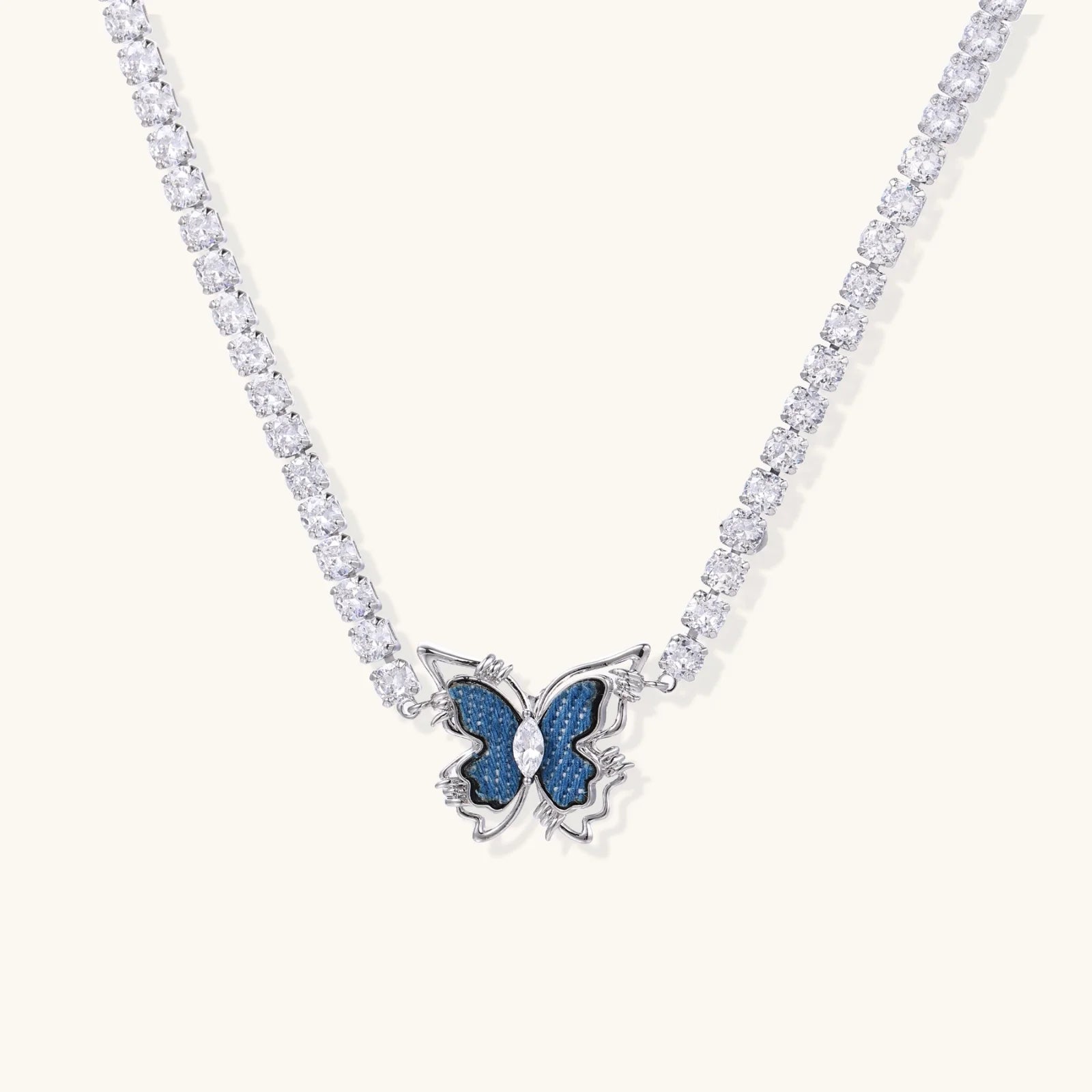 White gold plated tennis necklace with blue denim butterfly pendant and clear zirconia stones on cream background