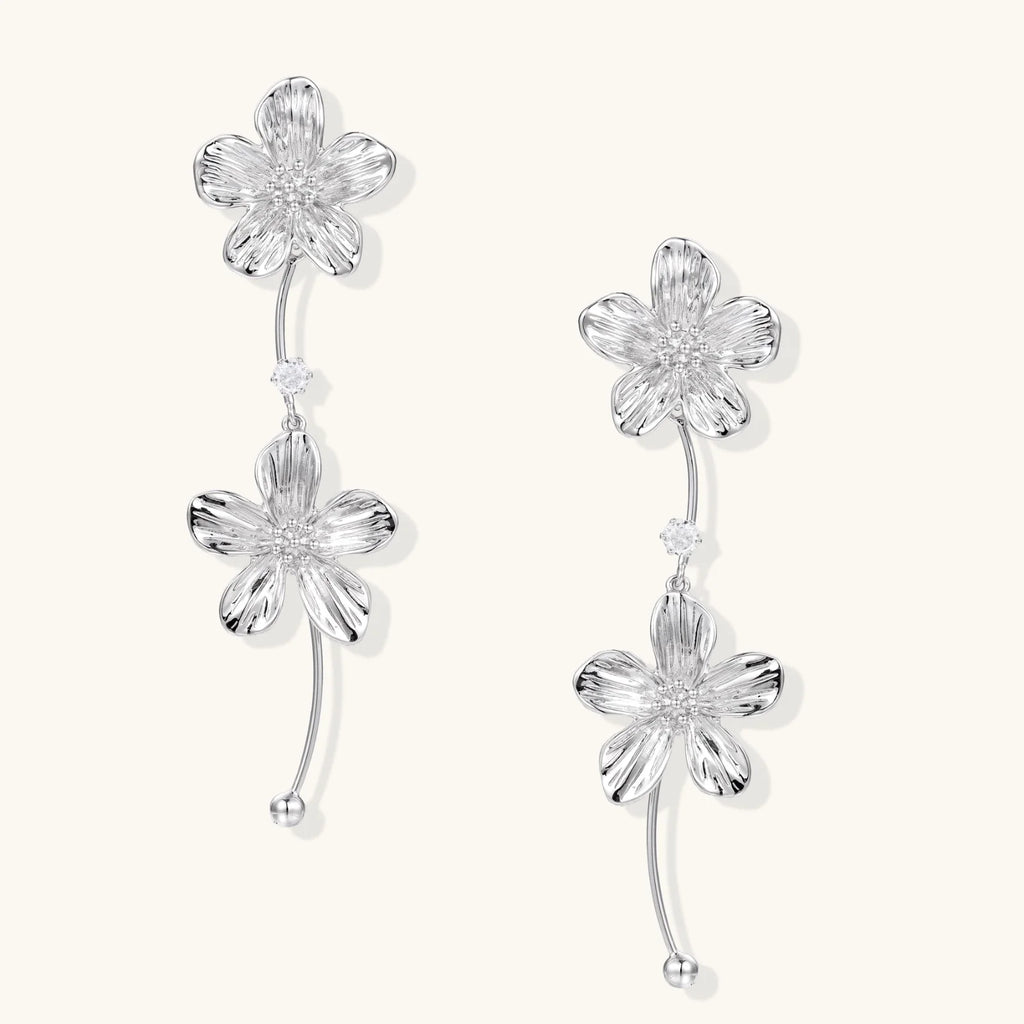 Silver-white asymmetric earrings with textured flower petals and crystal centers on cream background