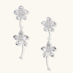 Silver-white asymmetric earrings with textured flower petals and crystal centers on cream background