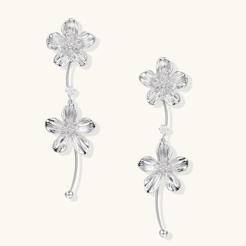 Silver-white asymmetric earrings with textured flower petals and crystal centers on cream background