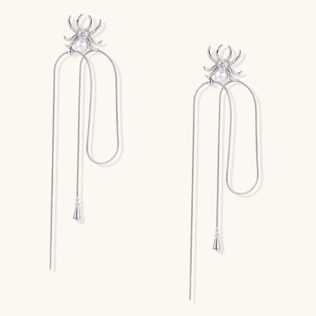White gold plated spider earrings with pearl body and long threader chains on beige background