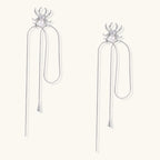 White gold plated spider earrings with pearl body and long threader chains on beige background