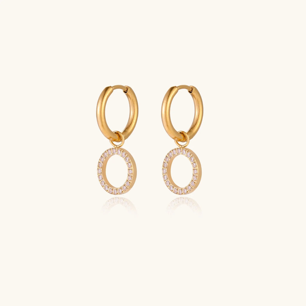 Gold-plated huggie hoop earrings with CZ-studded open circle charms on beige background