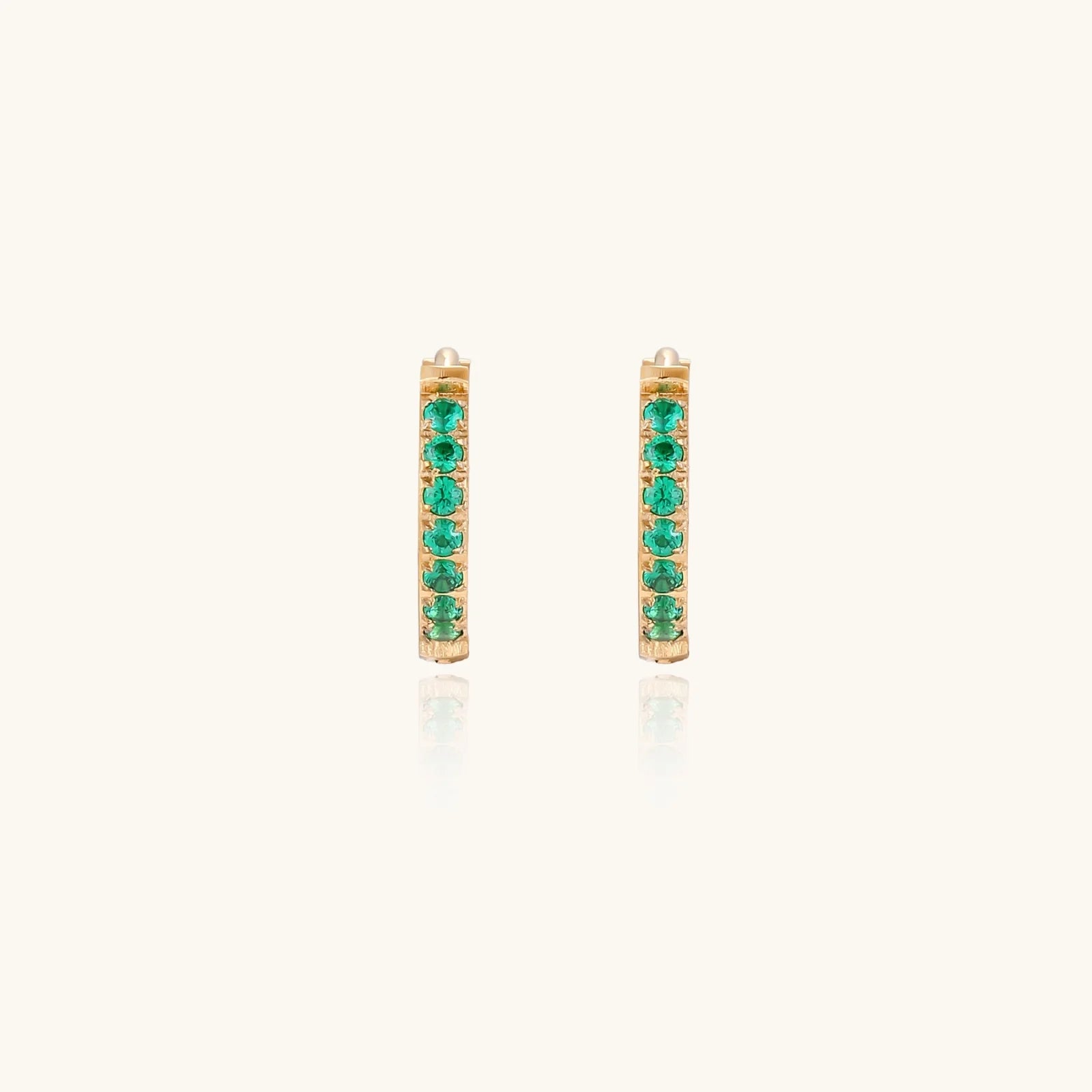 Pair of small gold huggie hoop earrings with bright green cubic zirconia stones on cream background