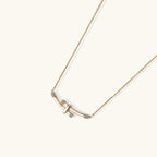 Gold-plated curved bar necklace with diamond accents on delicate chain against cream background