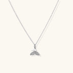Delicate white gold plated whale tail pendant with pavé crystals on silver chain against cream background.
