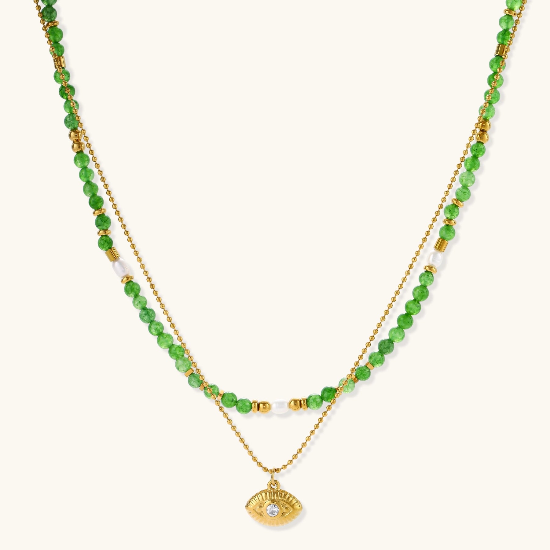 Layered necklace with green stone beads, gold spacers, white accents, and protective eye pendant on cream background.