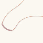 Rose gold jewelry set with pavé cubic zirconia stones including curved necklace, hoop earrings, and adjustable ring on cream background.