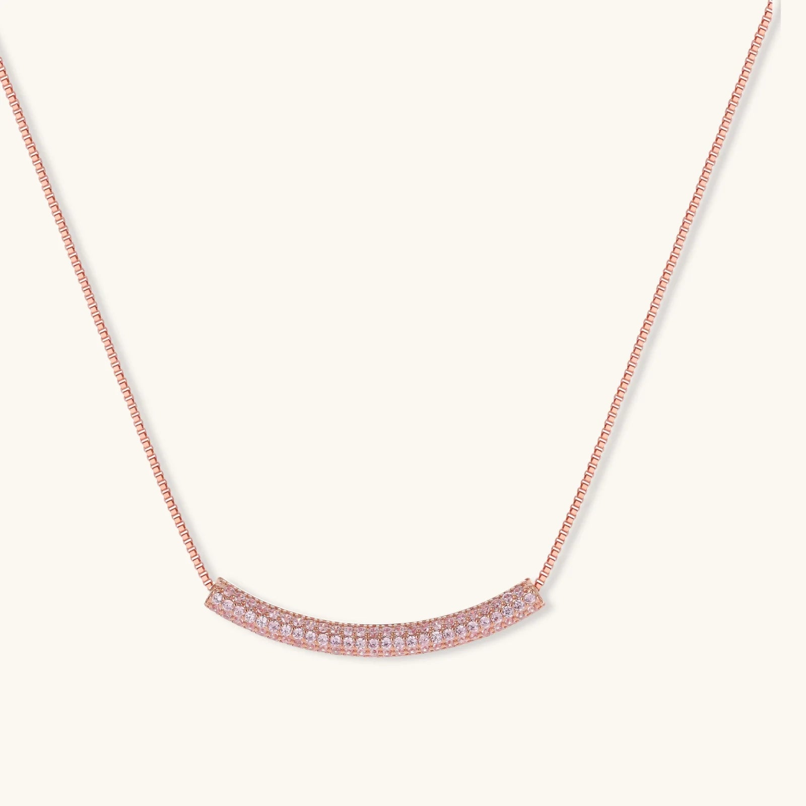 Rose gold jewelry set with pavé cubic zirconia stones including curved necklace, hoop earrings, and adjustable ring on cream background.