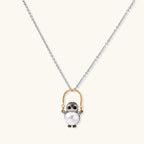 Whimsical owl pendant holding a white pearl on a gold swing, rhodium-plated silver chain on cream background.