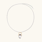 Whimsical owl pendant holding a white pearl on a gold swing, rhodium-plated silver chain on cream background.