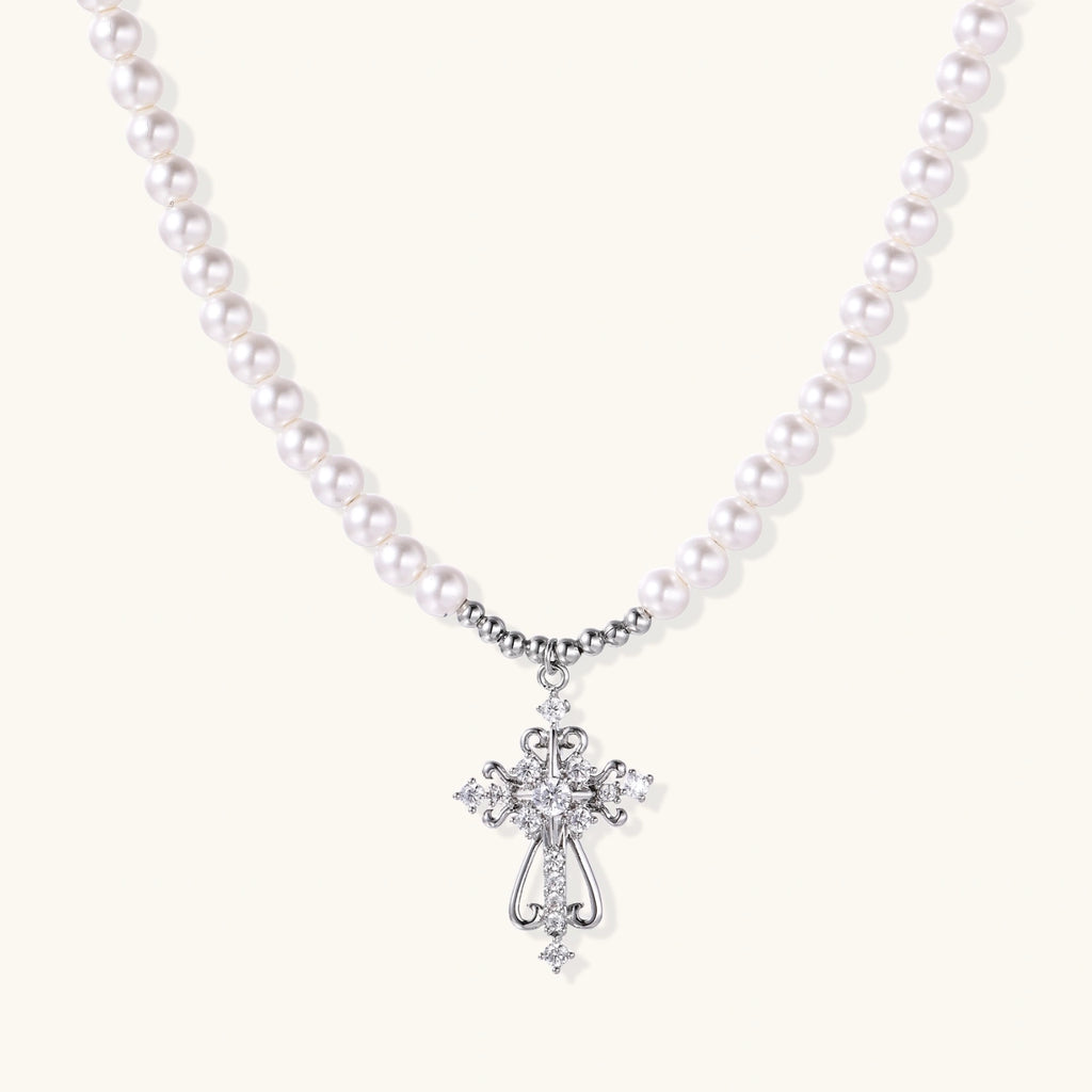 White pearl necklace with ornate silver cross pendant featuring zirconia crystals on cream background.