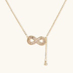 Gold infinity pendant with baguette crystals on adjustable chain against cream background.