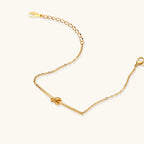 Delicate gold chain bracelet with minimalist bar and centered knot detail on cream background