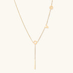 Gold Y-shaped necklace with L-O-V-E letter charms and vertical bar pendant on delicate chain against cream background