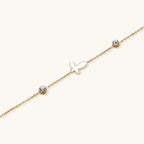 Gold chain bracelet with white mother of pearl butterfly pendant and two bezel-set crystals on cream background