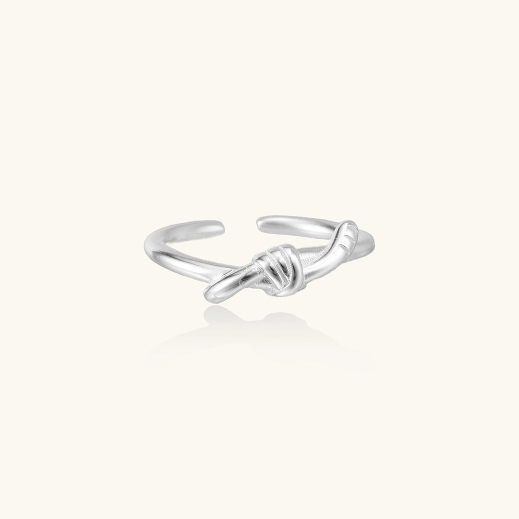 Delicate rhodium-plated silver ring with elegant knot design on cream background, adjustable band style