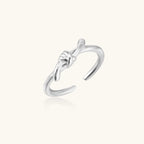 Delicate rhodium-plated silver ring with elegant knot design on cream background, adjustable band style